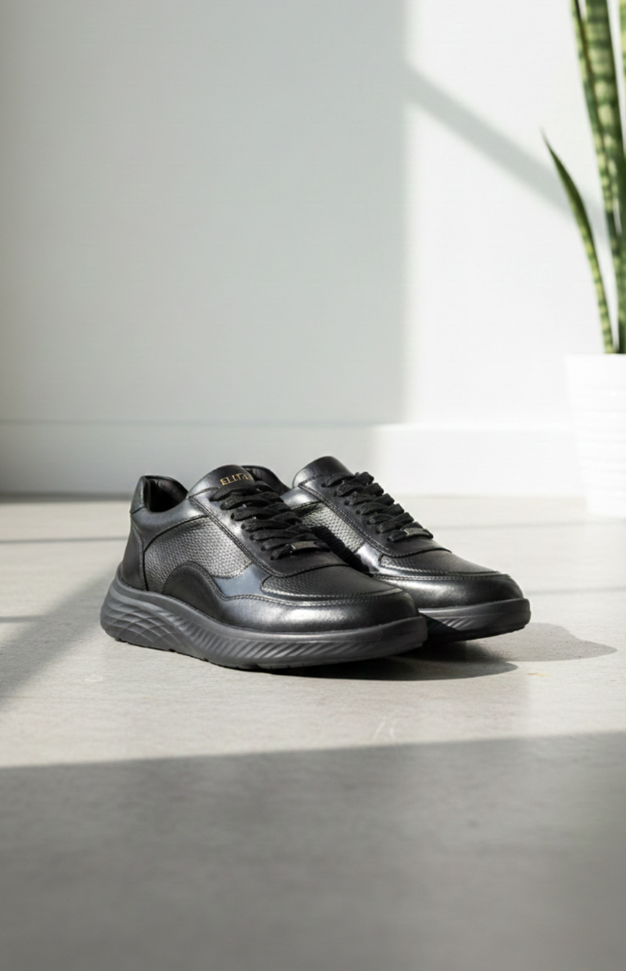 Baskets noires en cuir avec des lacets, présentées sur un sol clair.